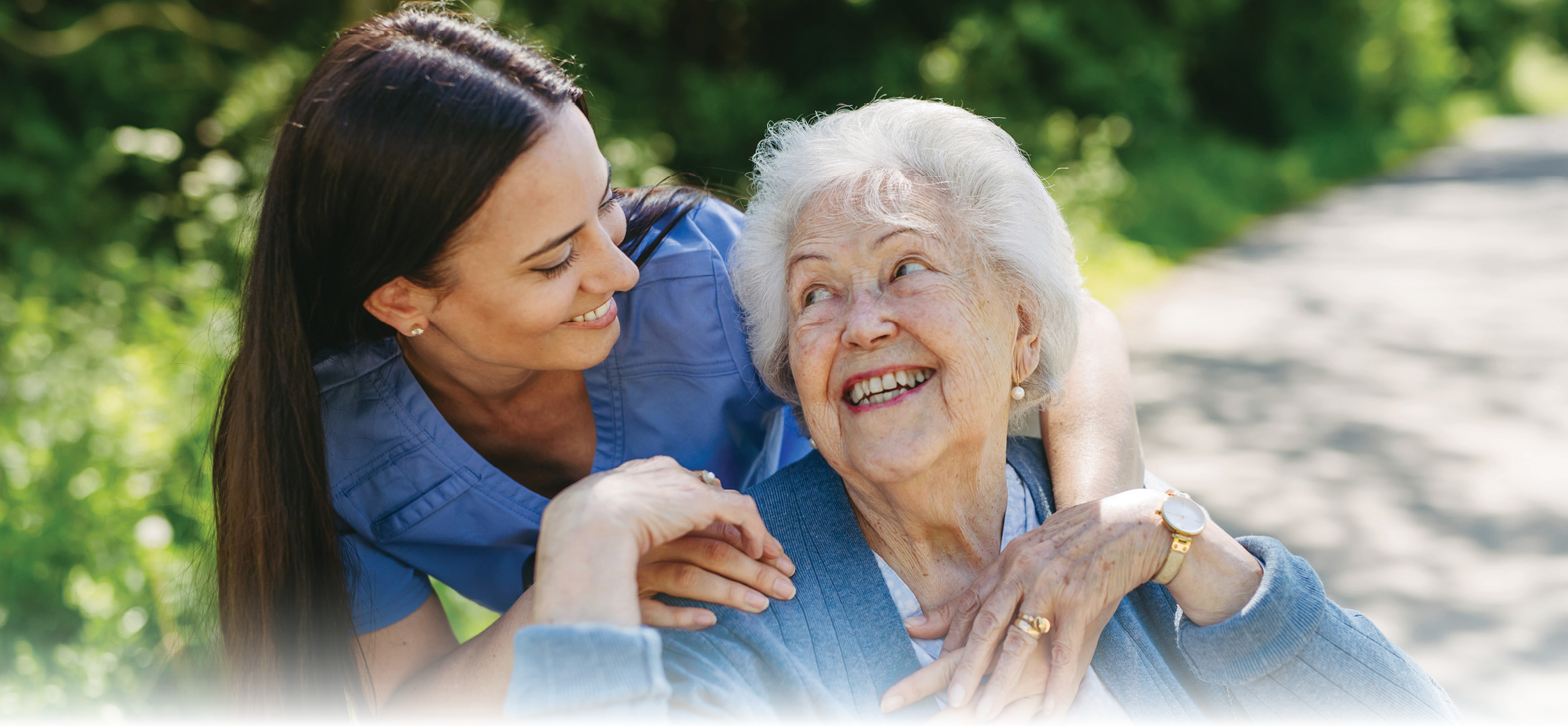 Caregiver pushing senior woman in wheelchair.